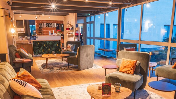 A spacious living area with a sofa, armchairs, and a coffee table. There is a bar area in the background with various items on display. - Golf Resort de Digne by Adonis (Digne-les-Bains)