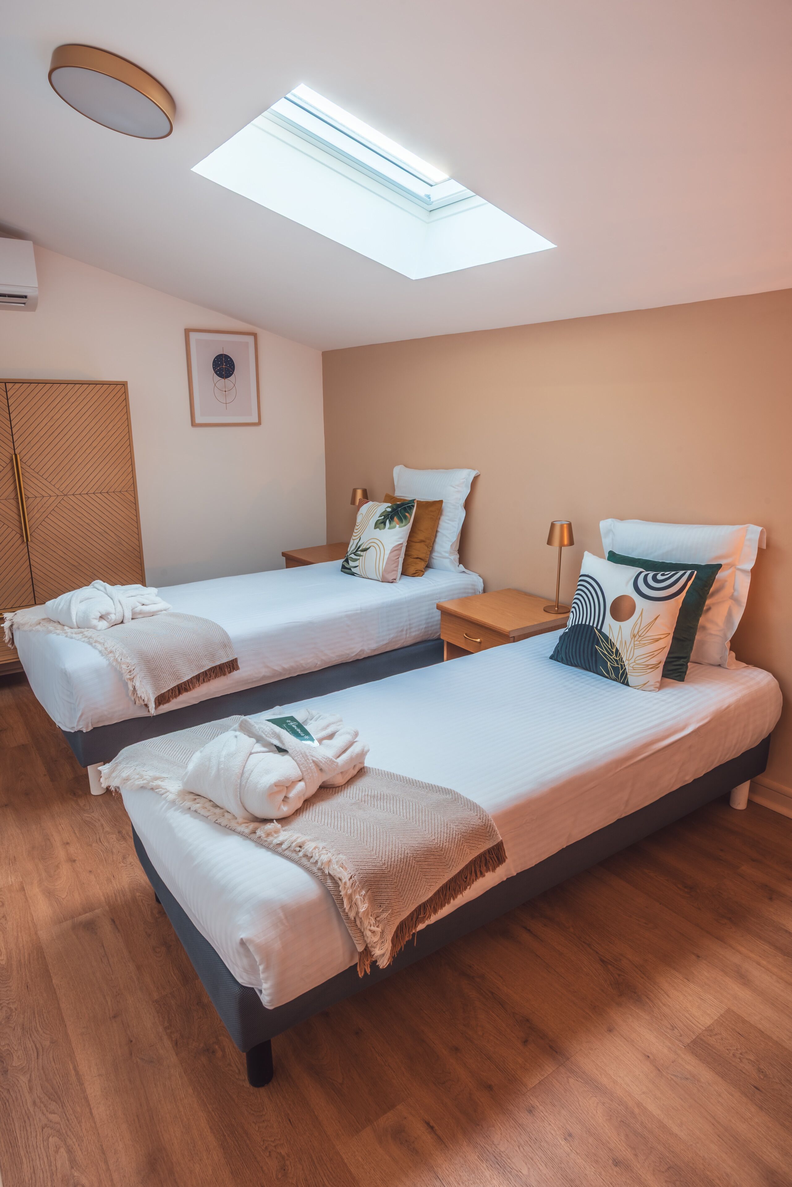 Une chambre d’hôtel avec deux lits, une lucarne, un tableau encadré au mur et un plancher en bois.