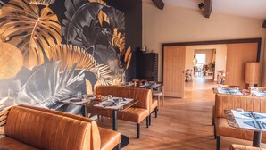A restaurant with leather booths, wooden tables, and a large tropical leaf mural on the wall. - Golf Resort de Digne by Adonis (Digne-les-Bains)