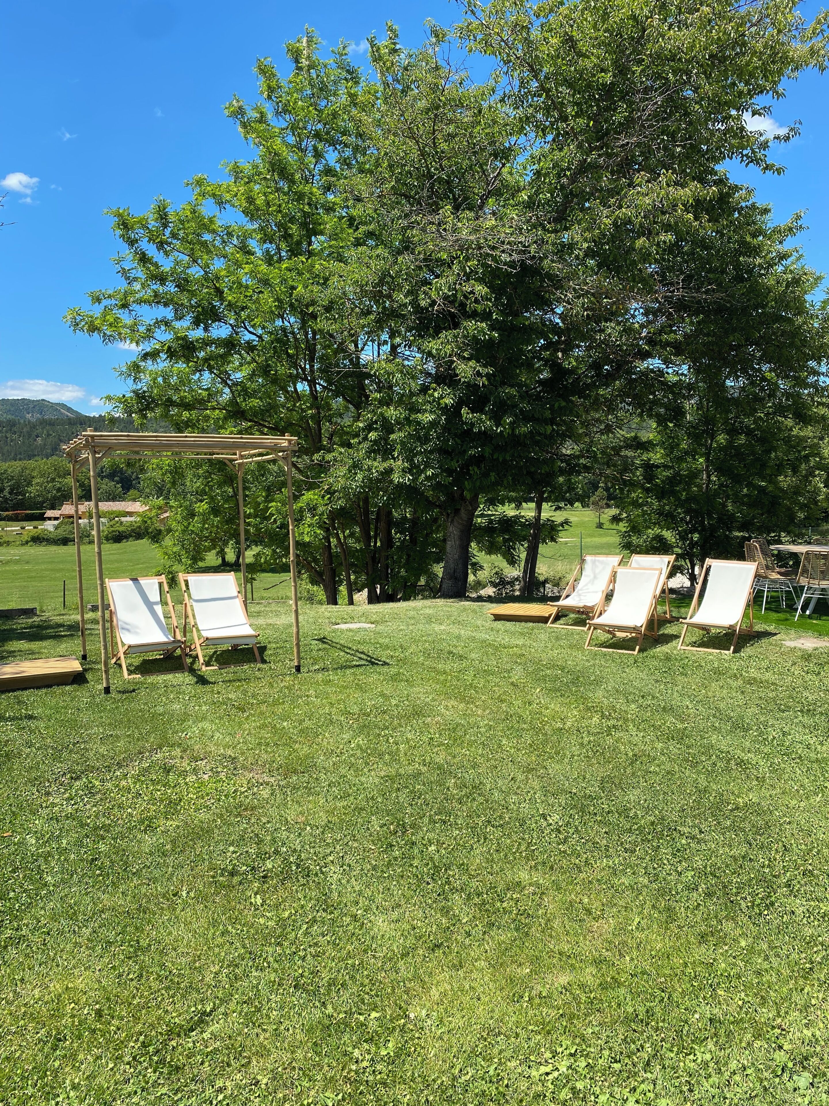 A grassy outdoor area with wooden pergolas and white lounge chairs.