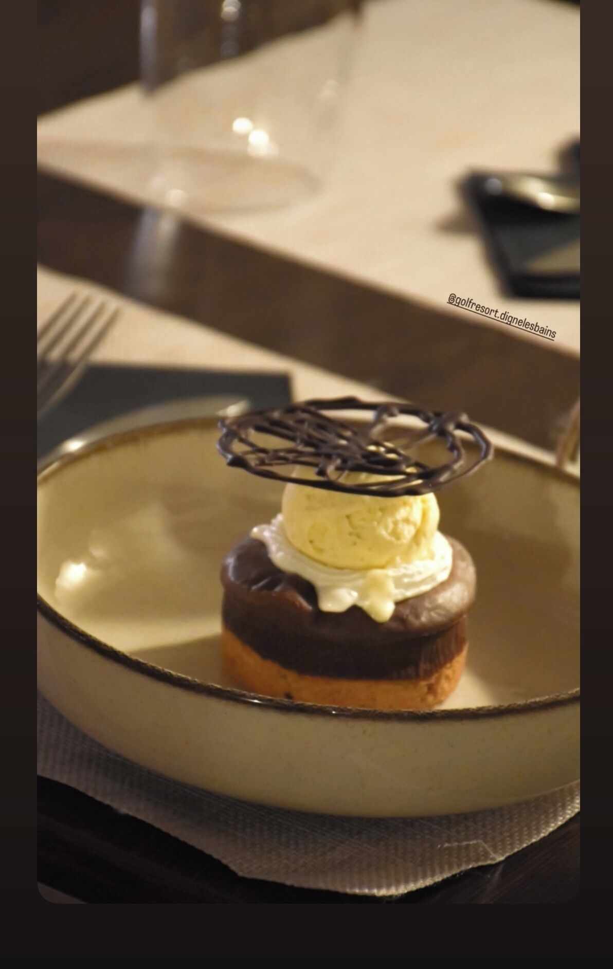 Un postre en un plato con base de chocolate, una bola de helado y decoración de chocolate.