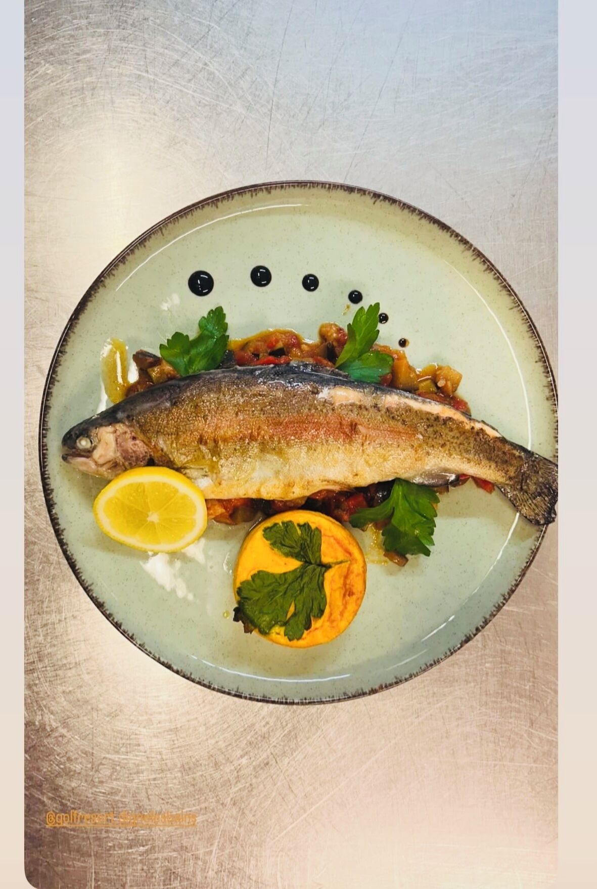 A plate with a whole fish, lemon slice, and parsley garnish.