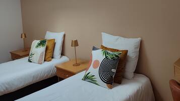 Habitación de hotel con dos camas individuales, cada una con mesita de noche y lámpara. La habitación tiene un tragaluz y paredes color beige.