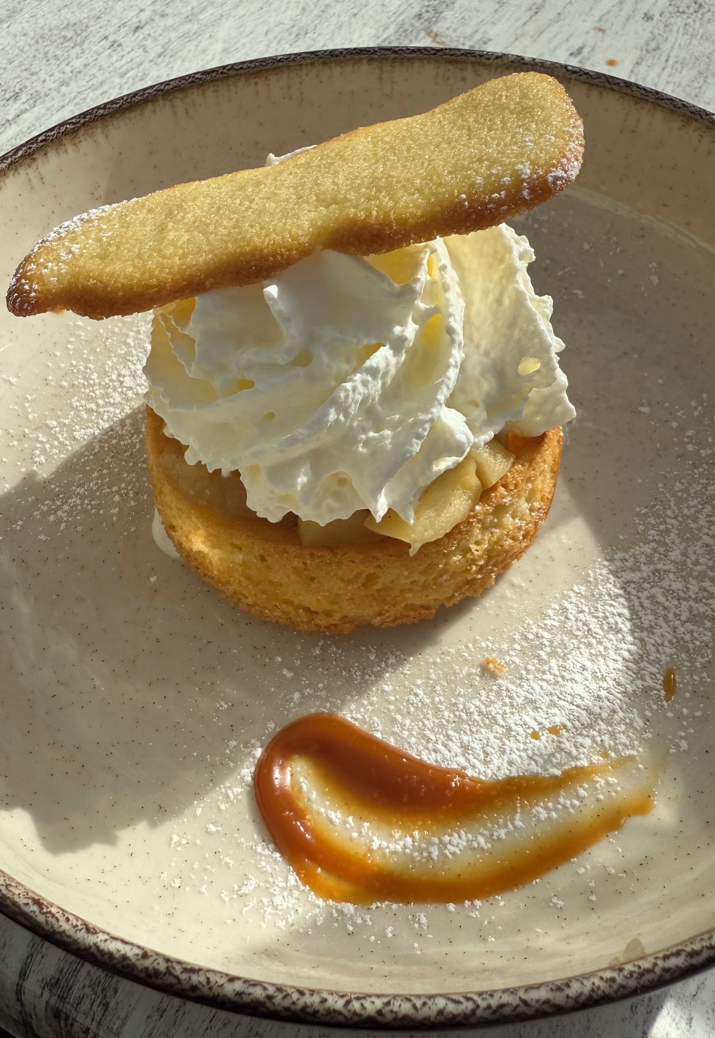 Postre con crema batida y salsa de caramelo sobre un plato.