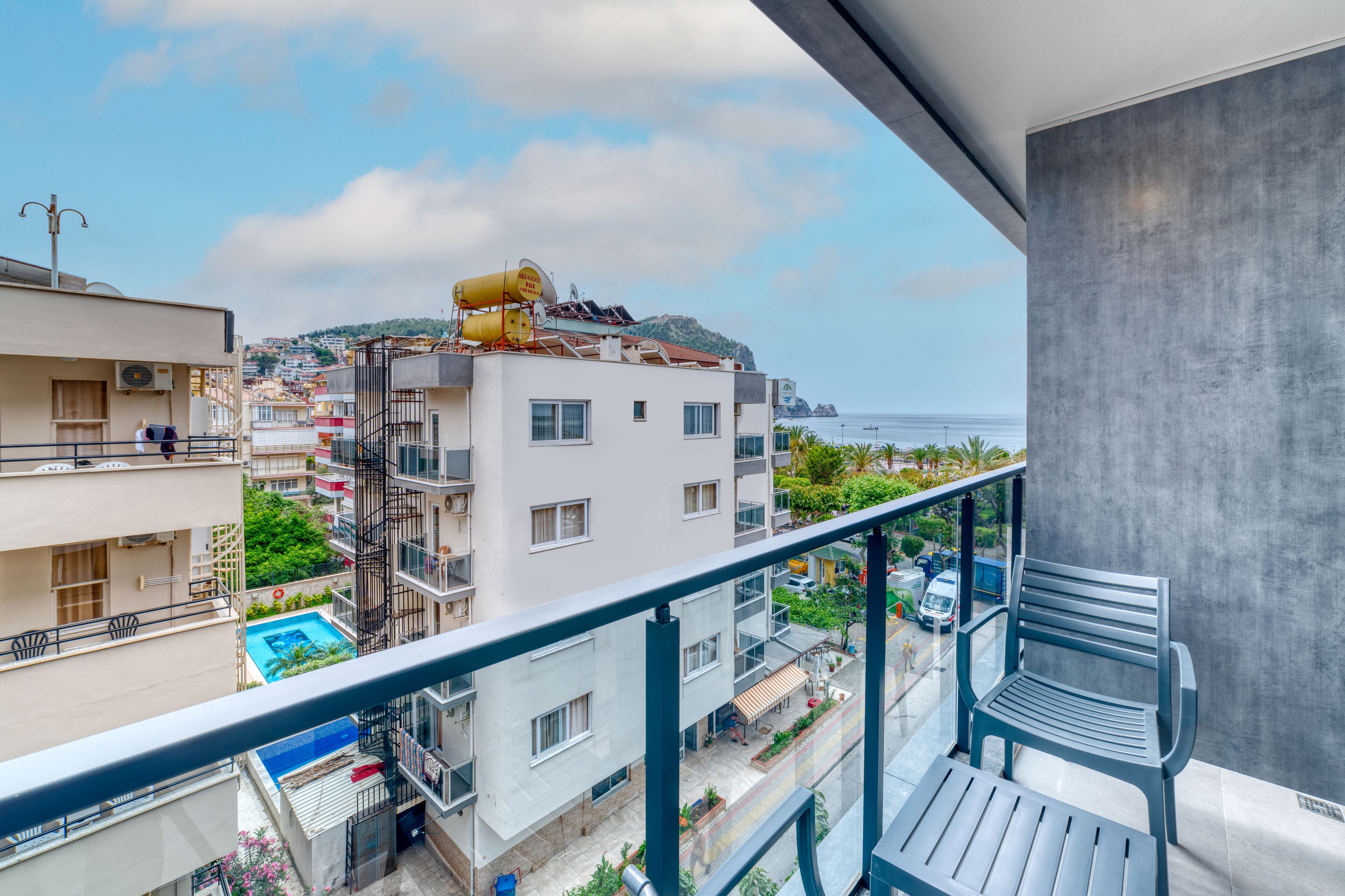 A balcony with a view of a residential area, a swimming pool, and a distant coastline.