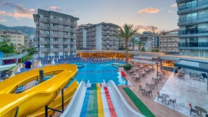 Área de piscina en un resort con varias toboganes, sillas de descanso y mobiliario exterior.