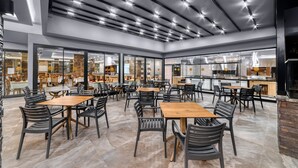 Un amplio comedor interior con varias mesas y sillas, un diseño moderno de techo y un área de cocina visible al fondo.