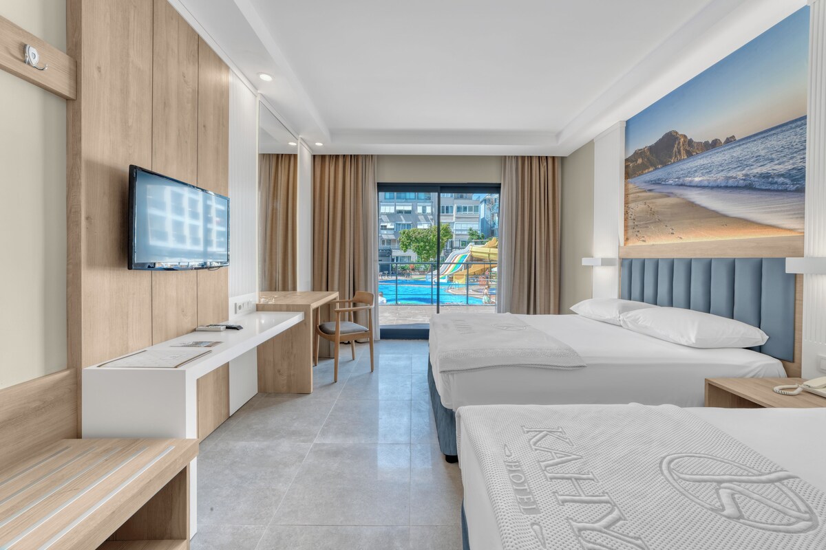 Habitación de hotel con televisión, escritorio, silla, cama y vistas a una piscina y edificios.