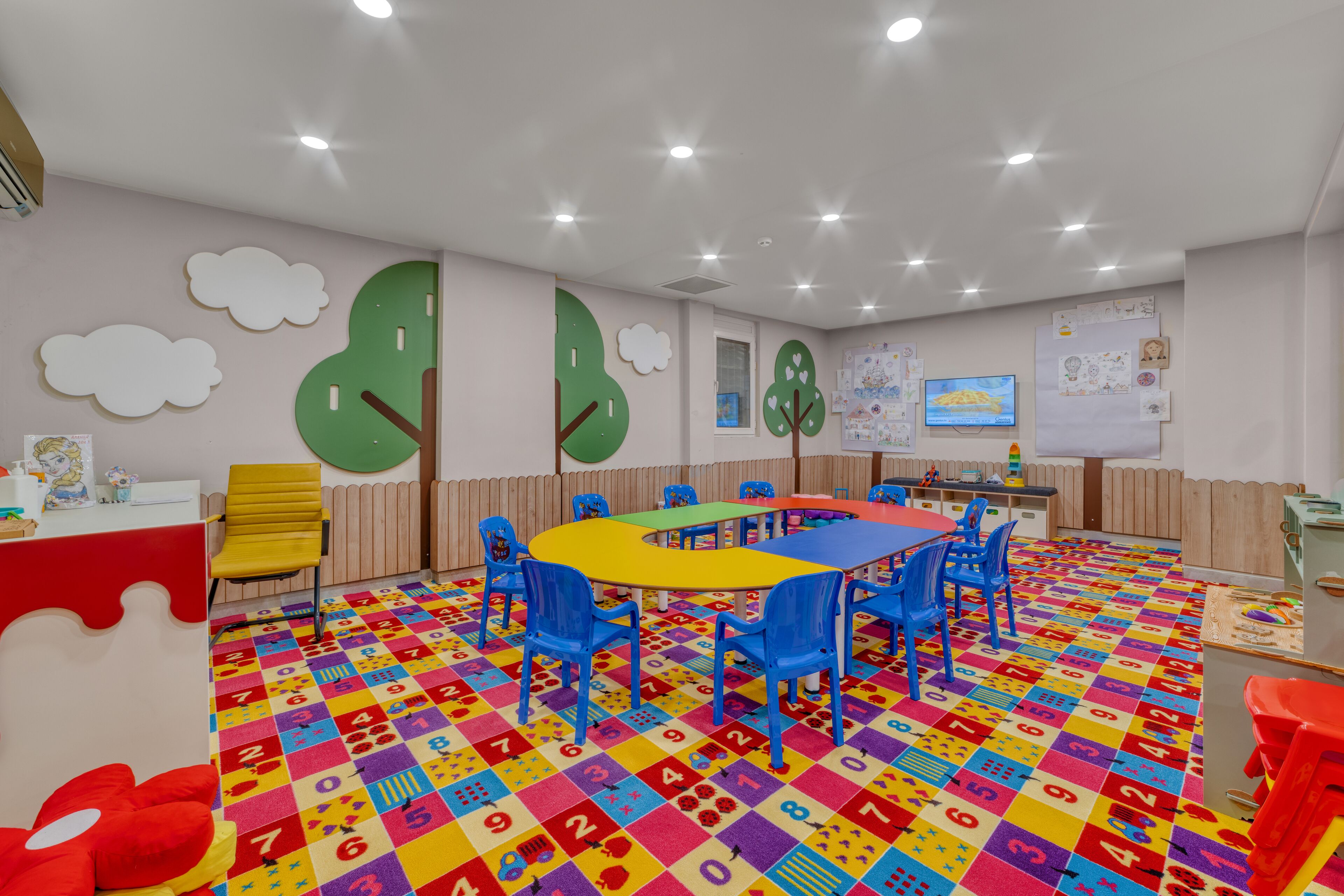 Una sala de juegos infantil con mobiliario colorido y una alfombra con motivos de números.