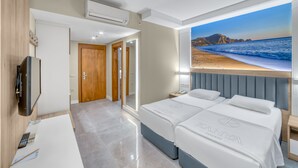 Habitación de hotel con dos camas, un televisor, un escritorio con un control remoto y documentos, y vista al mar.