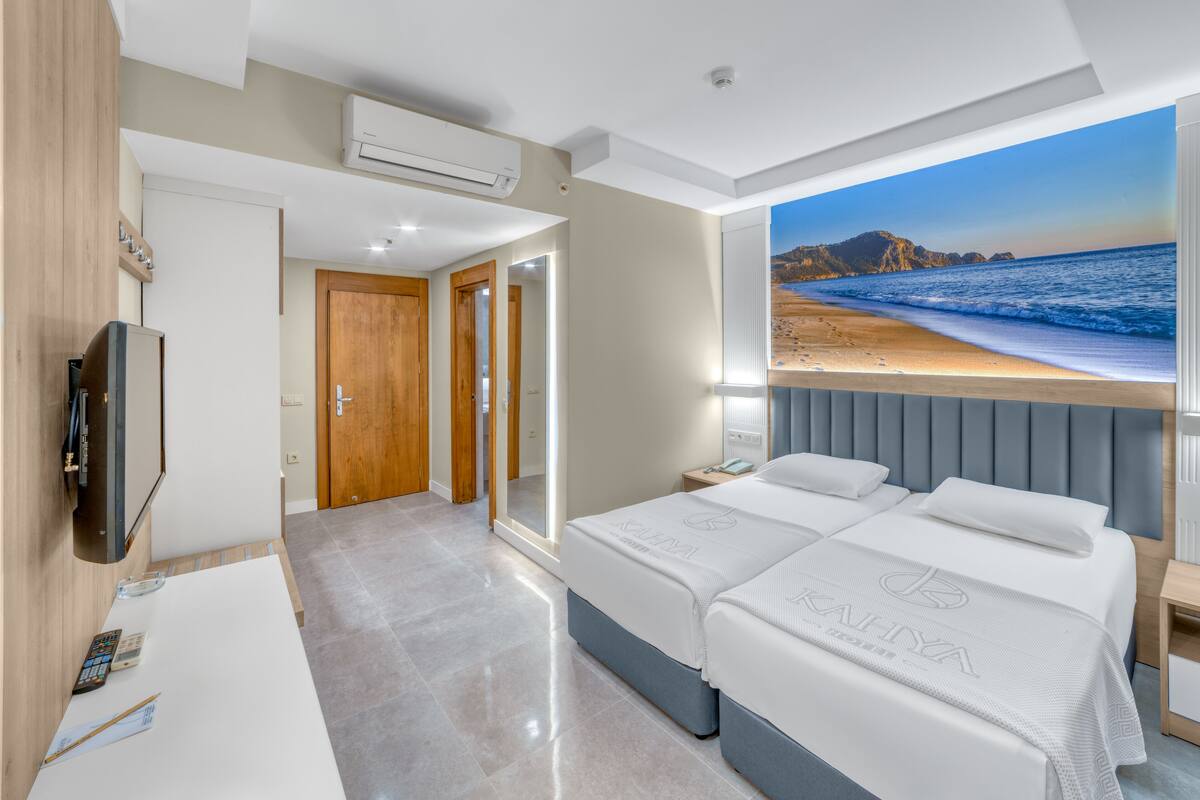A hotel room with two beds, a TV, a desk with a remote and papers, and a beach view.