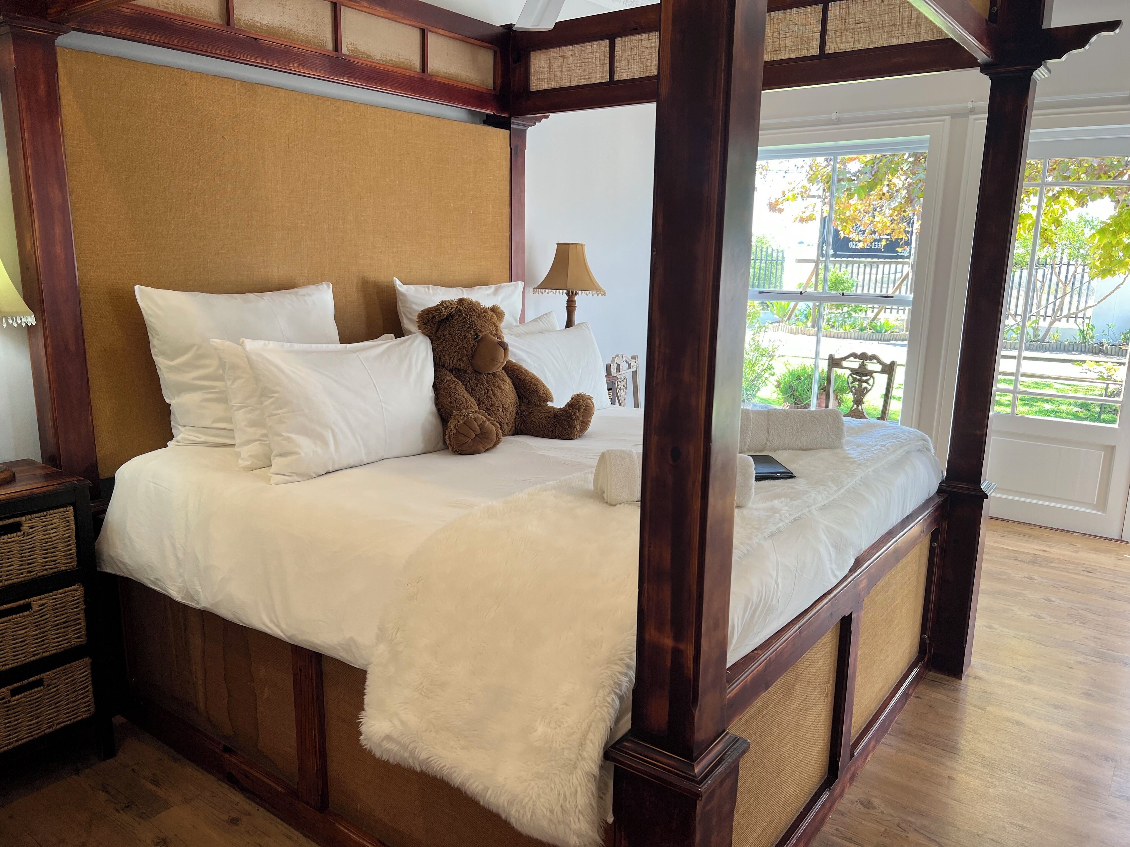 A four-poster bed with white bedding and a teddy bear.