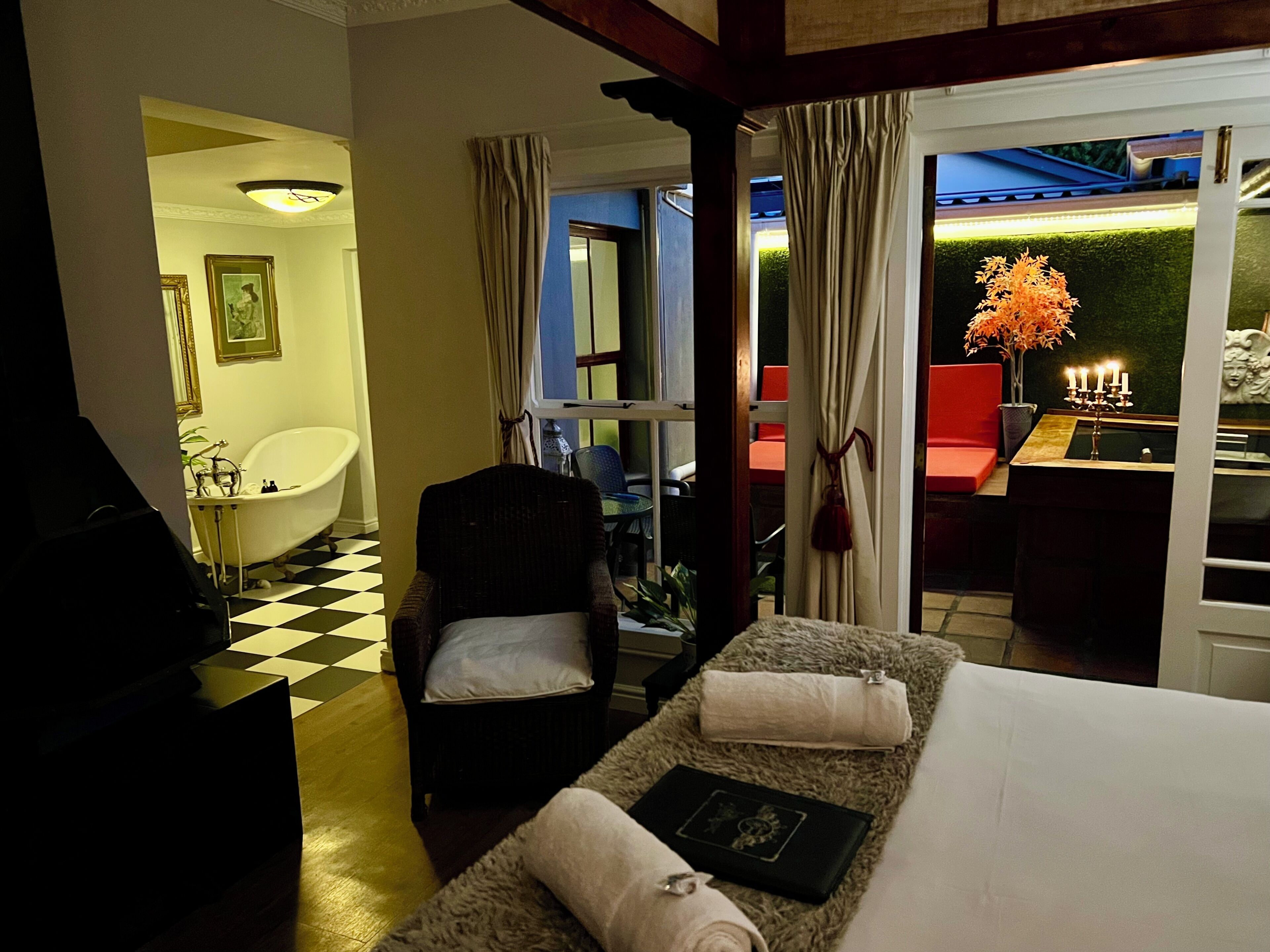Une chambre d’hôtel avec un sol à carreaux, une baignoire, une chaise, un lit avec des serviettes, une table avec un chandelier et une vue sur l’extérieur.
