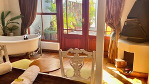 Une salle de bain avec une baignoire, une chaise en bois, un lit et une fenêtre avec des rideaux.