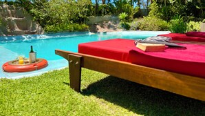 Un salon au bord de la piscine avec un banc rouge rembourré, une bouteille de champagne et un verre de jus d’orange sur un plateau.