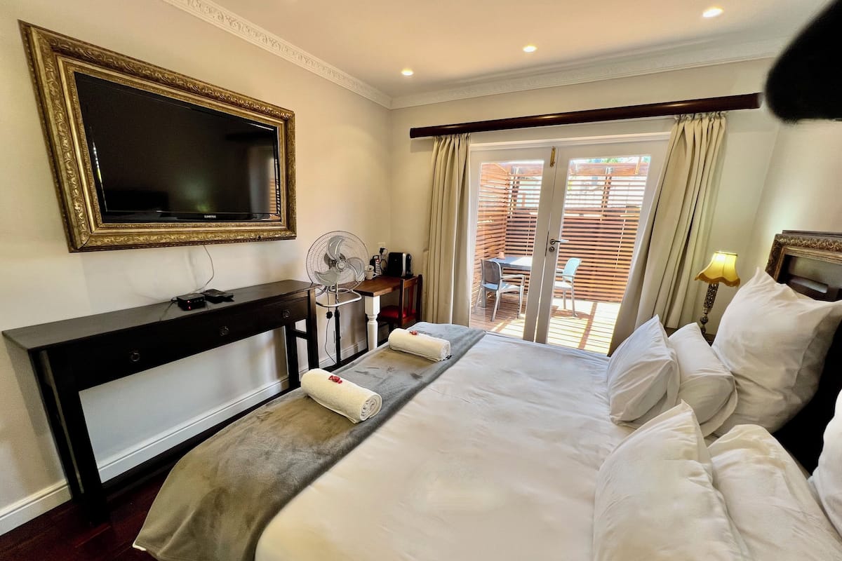 A hotel room with a bed, a desk, a chair, a fan, and a television.