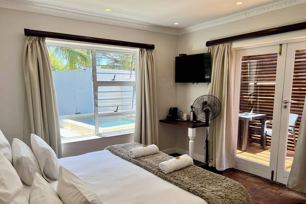 A hotel room with a bed, a desk with a fan, a TV, and a view of a pool.