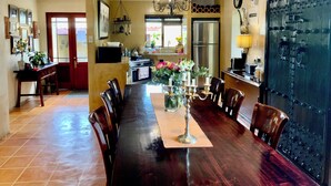 A spacious dining area with a long table, chairs, a chandelier, and a kitchen in the background. - Goblin's Mead (Cape Town)
