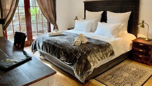 A neatly made bed with white linens, a dark headboard, and a bedside lamp. - Goblin's Mead (Cape Town)