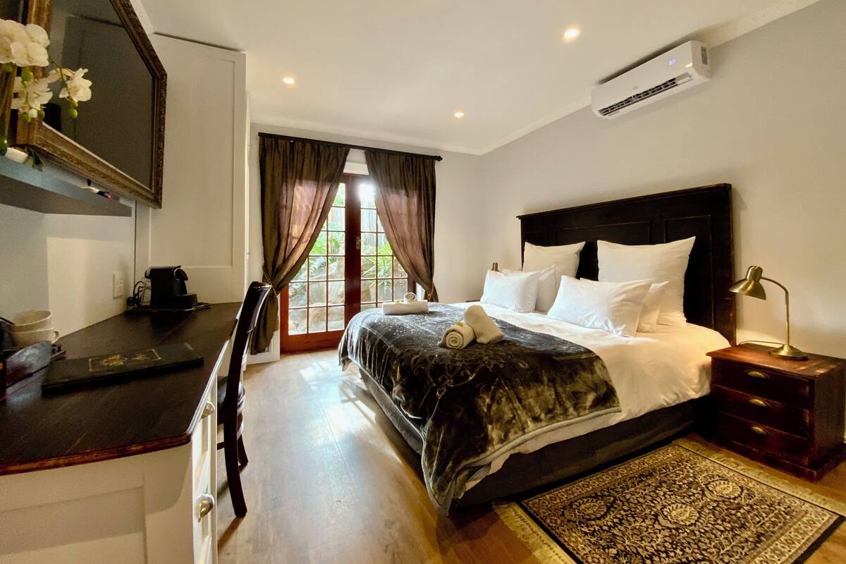 A hotel room with a bed, bedside table, desk, chair, and a large mirror.