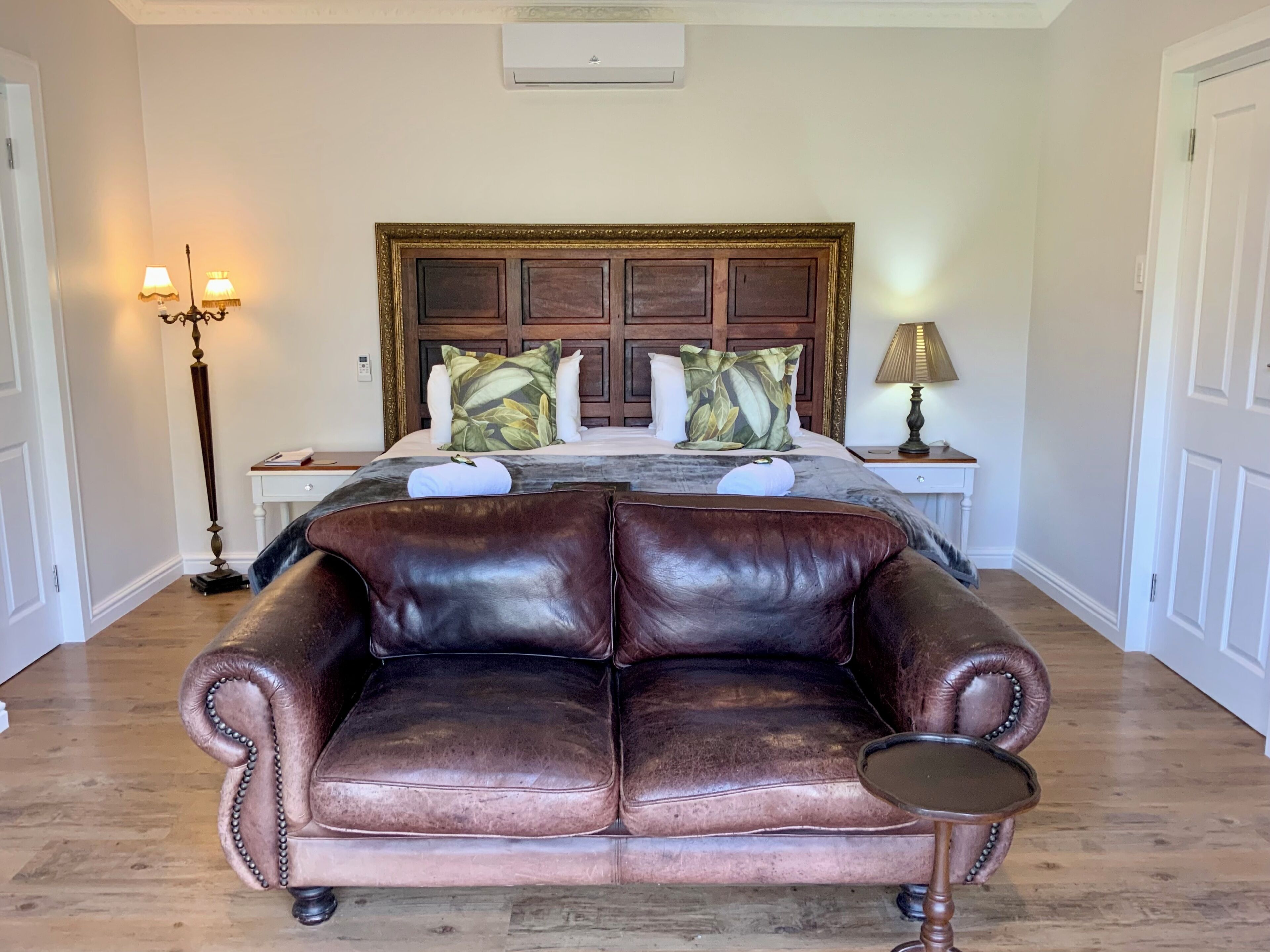 A bedroom with a large bed, a leather sofa, a nightstand, and a floor lamp.