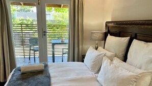 A hotel room with a bed, a nightstand, a lamp, and a view of an outdoor patio with a table and chairs. - Goblin's Mead (Cape Town)
