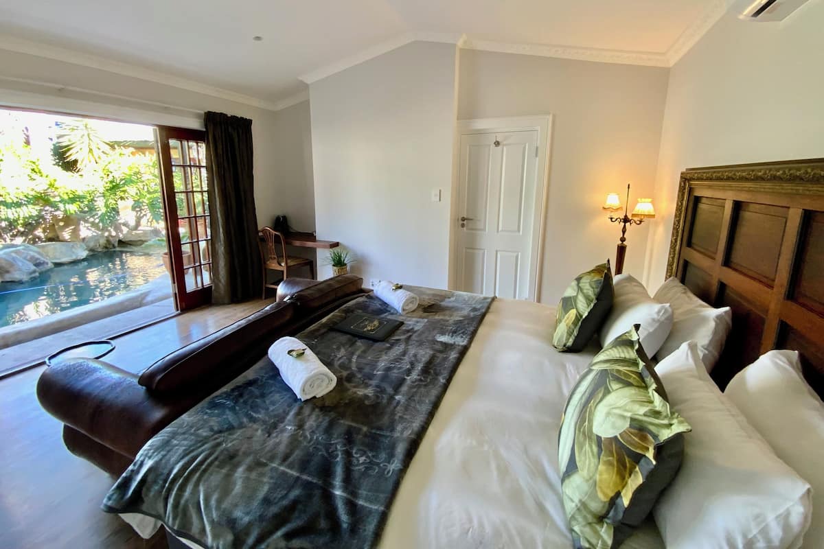 A hotel room with a bed, a desk, a chair, a window with a view of a pool, and a door.
