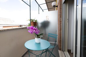 A balcony with a round table, a chair, and a potted plant with purple flowers. - Roof Garden Zaccardi (Rome)