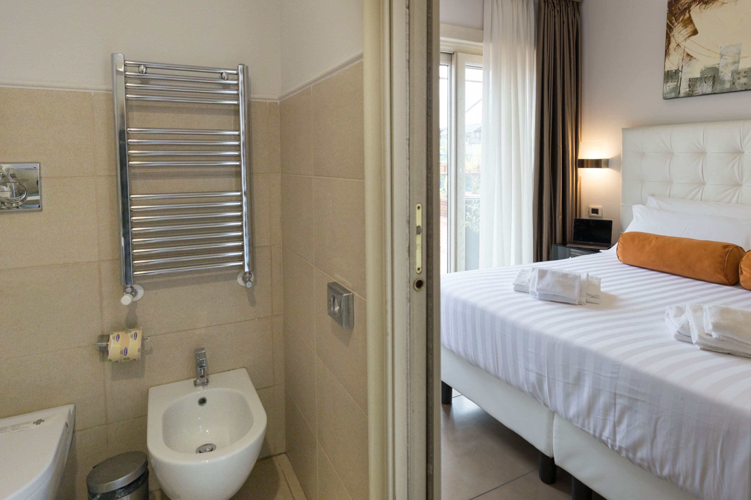 Una habitación de hotel con cama, mesita de noche con lámpara, un bidé y un perchero para toallas.
