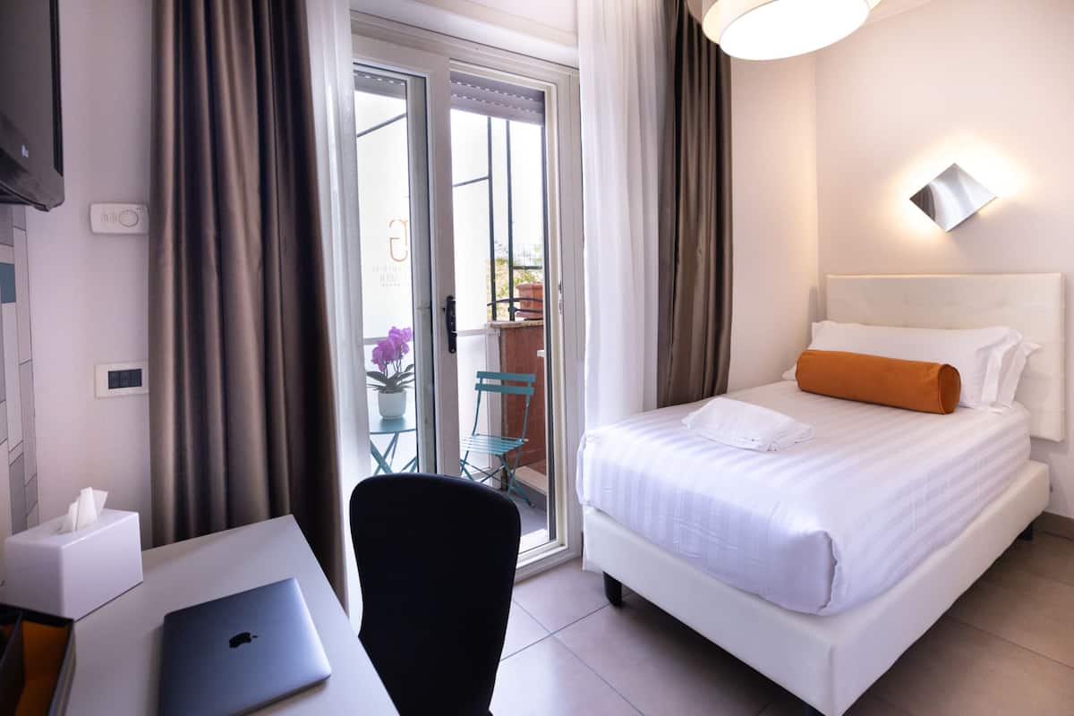 Habitación de hotel con cama, escritorio con computadora portátil, silla, mesita de noche con caja de pañuelos y ventana con cortinas.