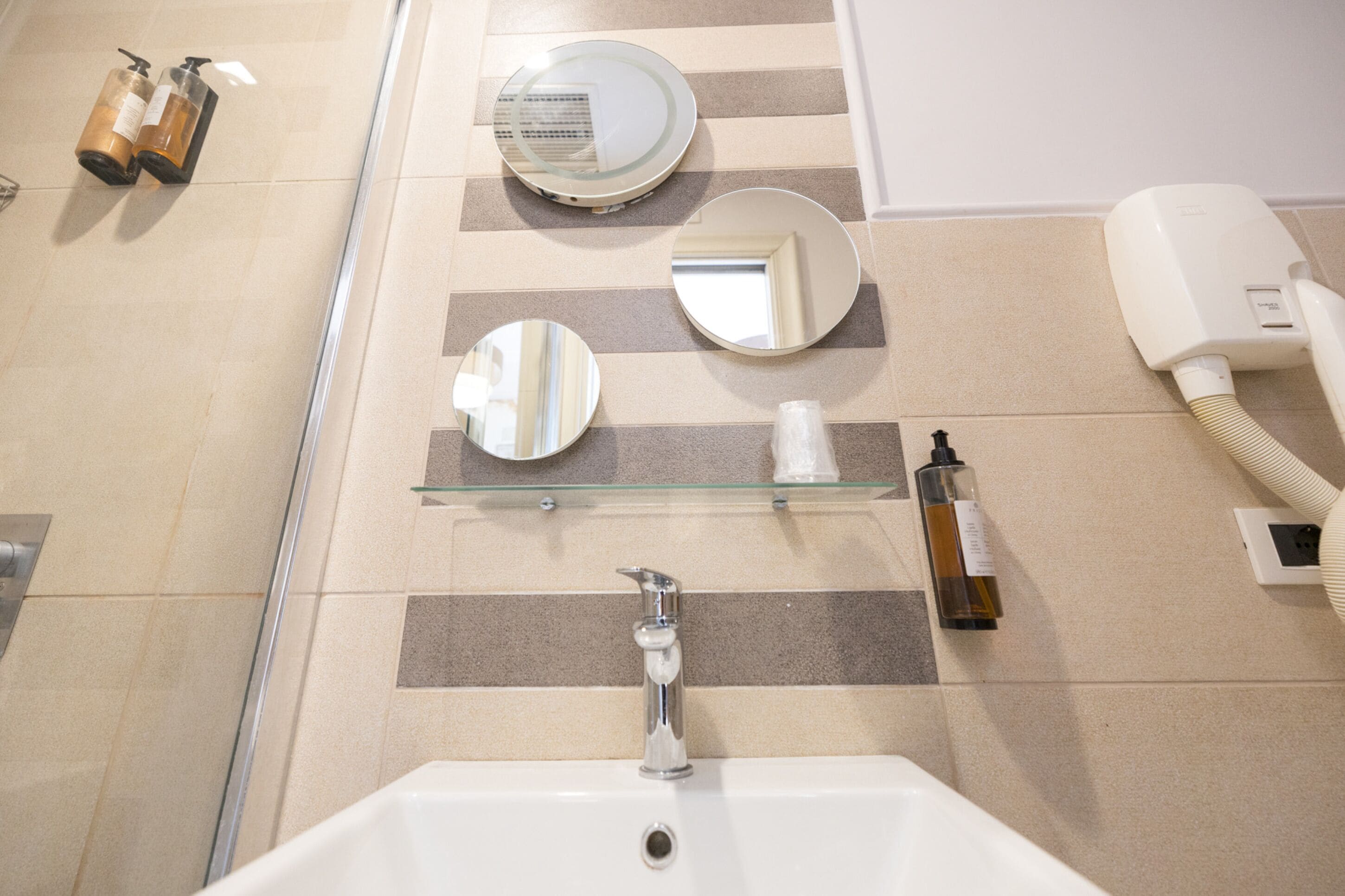 A bathroom with a sink, mirrors, and toiletries on a shelf.