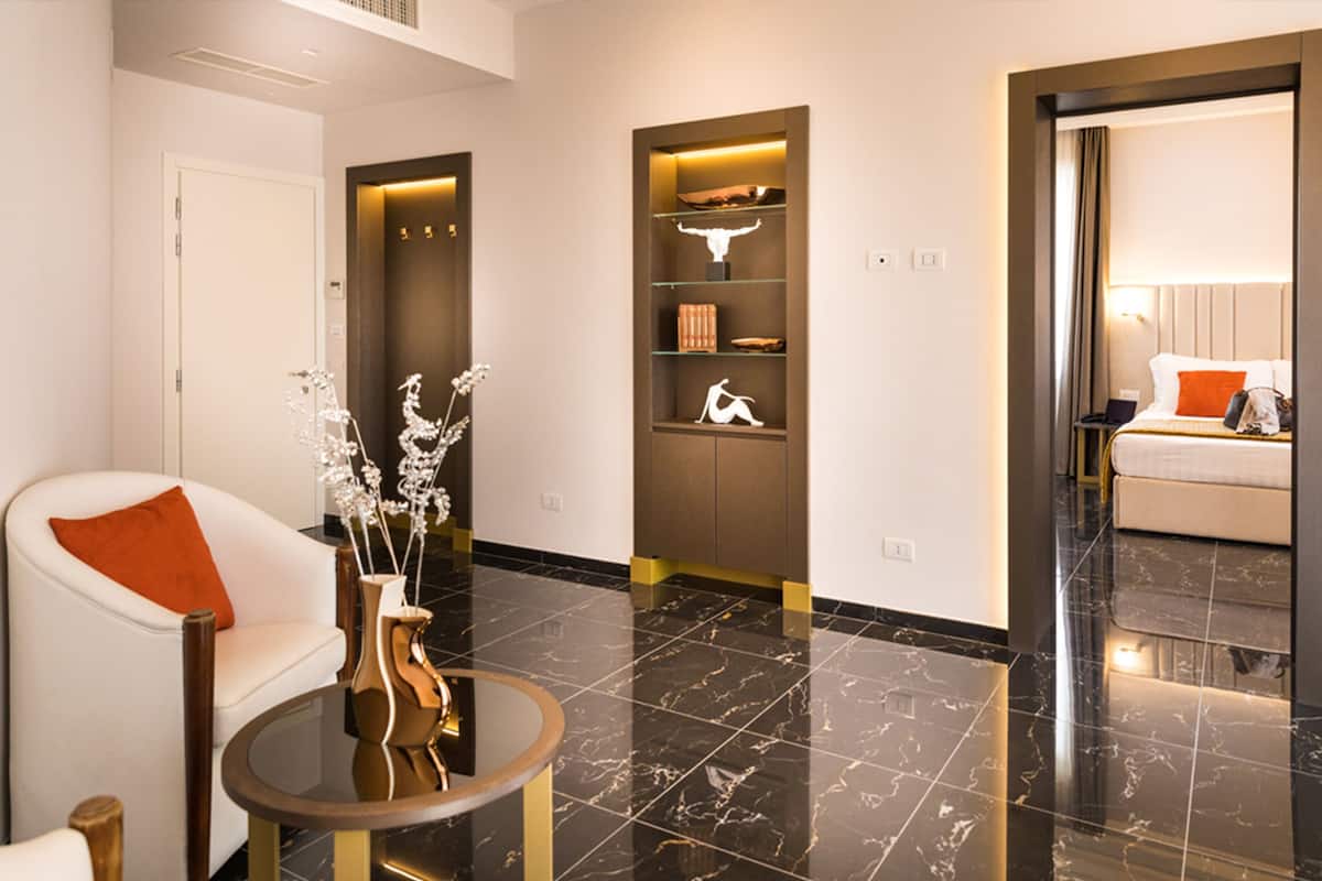 A modern hotel lobby with a marble floor, a seating area with a white chair and a round table, and a bookshelf with decorative items.