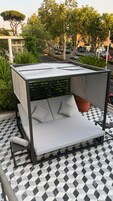 A rooftop lounge with a metal frame, cushioned seating, and a patterned floor.
