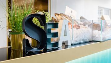 Een receptiebalie met een groot bord waarop 'SEA' staat, een potplant en een glazen vitrine met objecten.