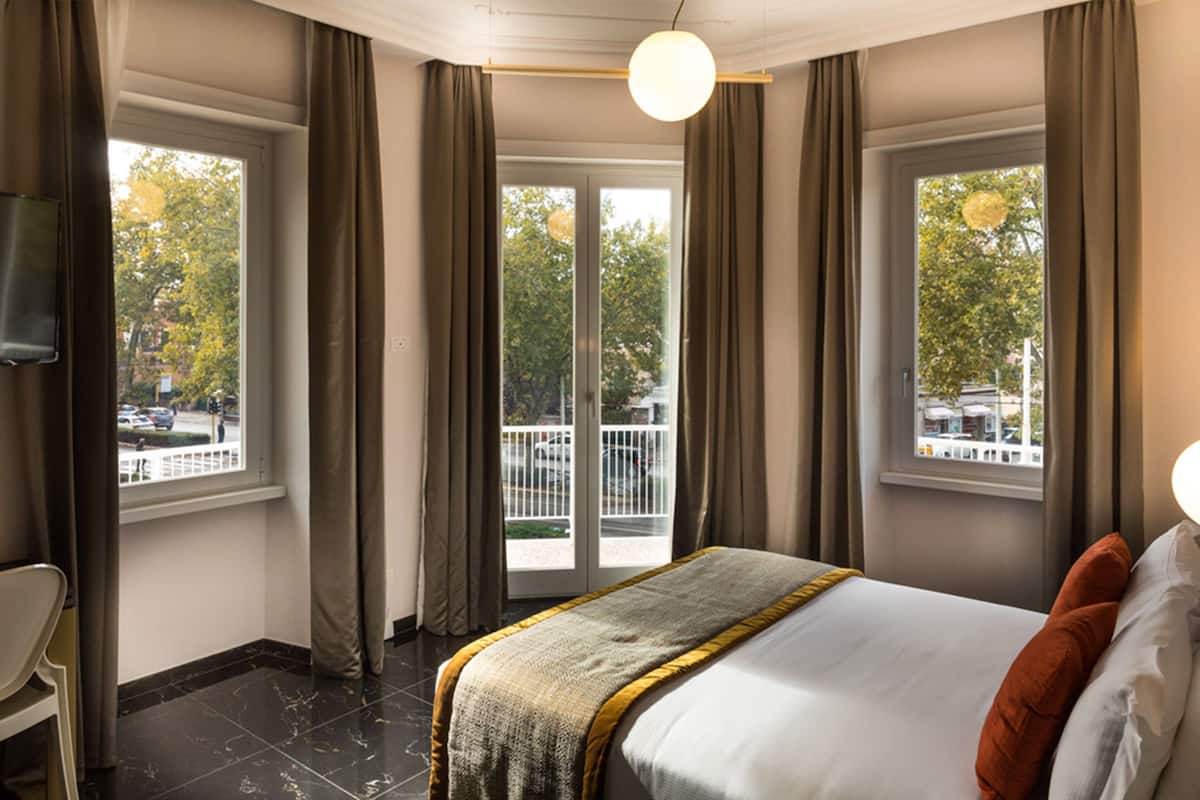 A hotel room with a bed, a chair, and a balcony with a view of the street.