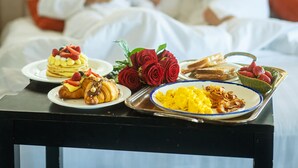 A breakfast setup with pancakes, croissants, and scrambled eggs on a tray, with a bed and two people in the background. - Hotel Villa Zaccardi (Rome)