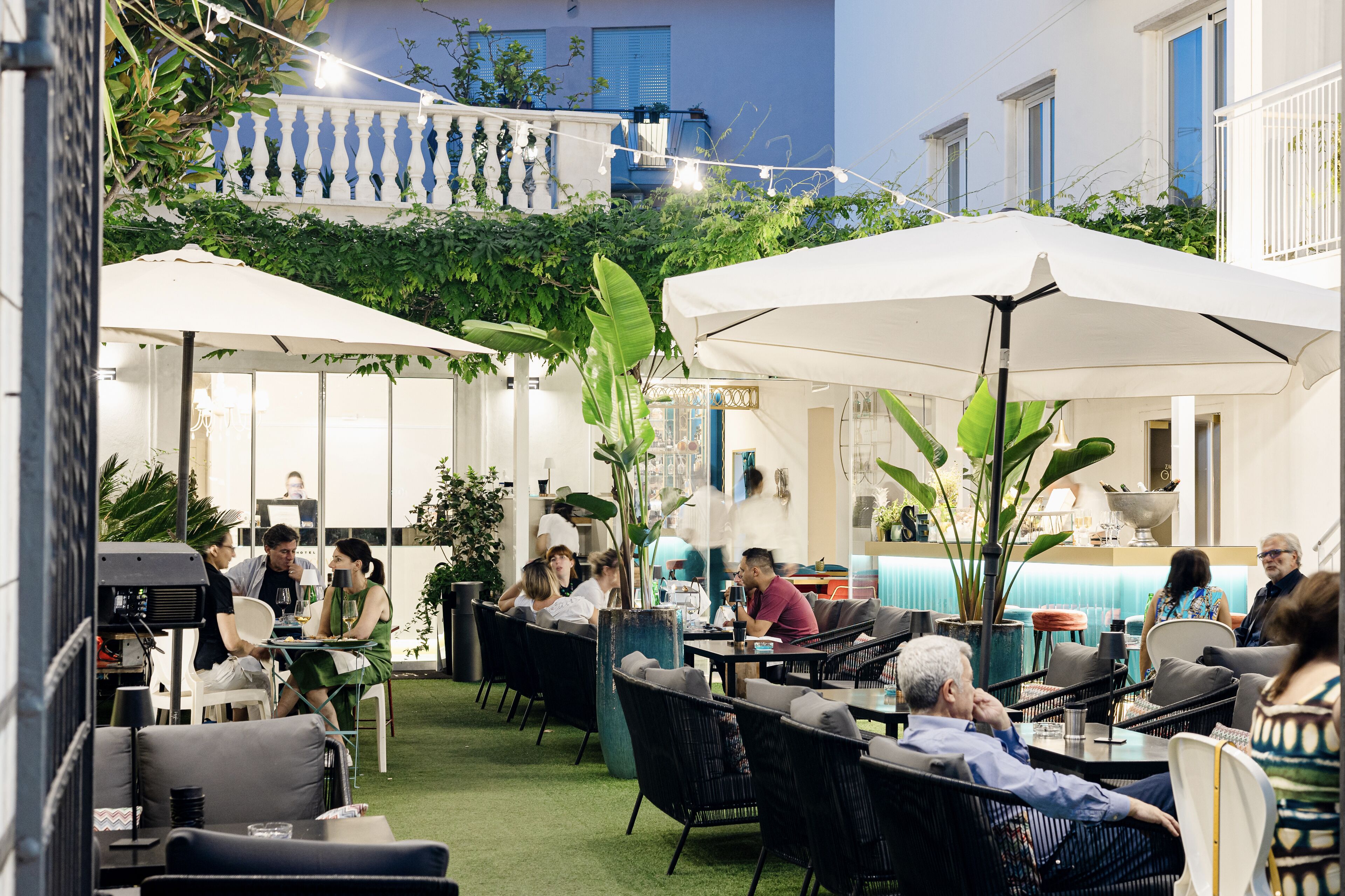 Een terras met tafels en stoelen, omgeven door groen en parasols.
