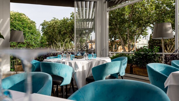 An outdoor dining area with tables and chairs, large windows, and greenery visible through the windows. - Hotel Villa Zaccardi (Rome)