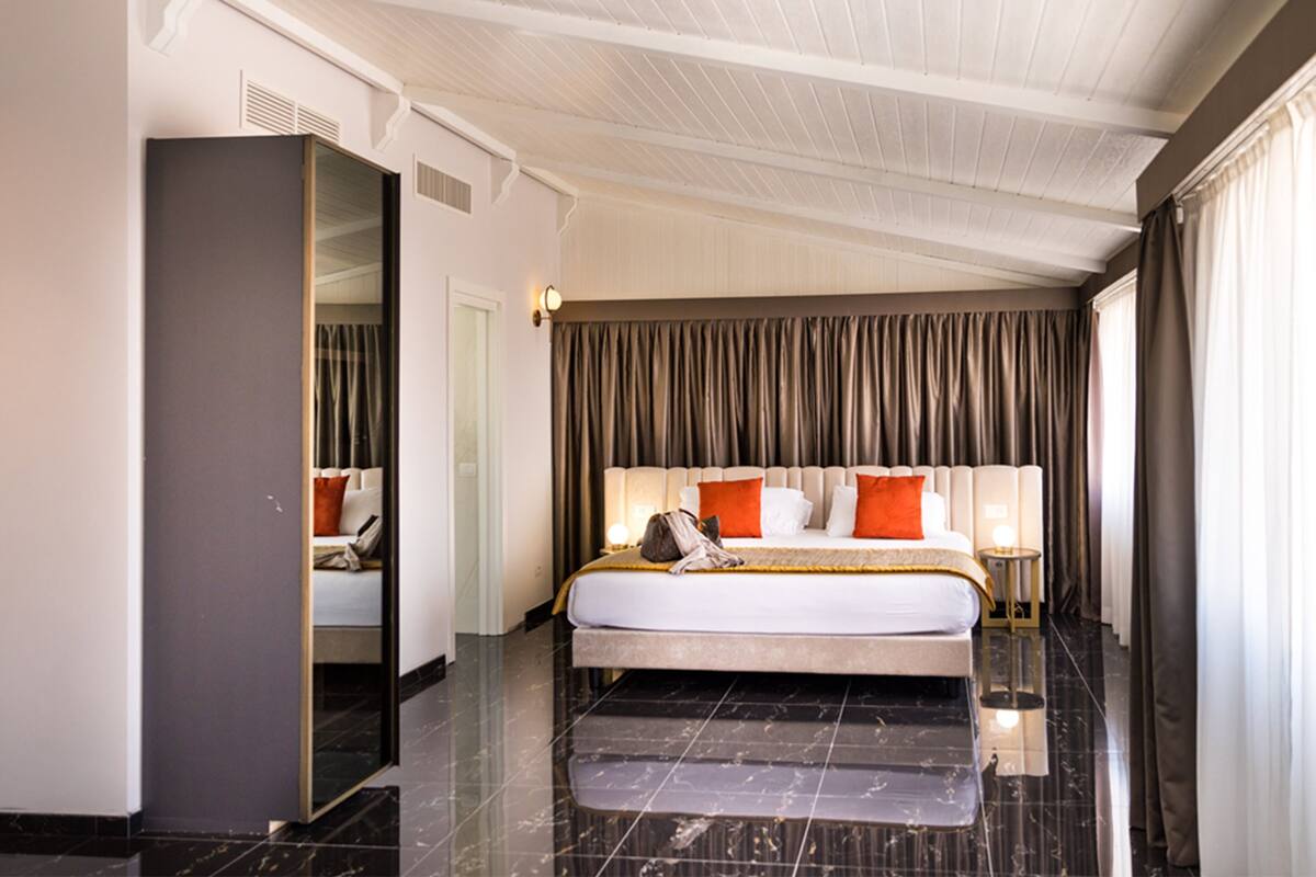 A modern hotel room with a large bed, a mirror, a nightstand, and a view of the outdoors.