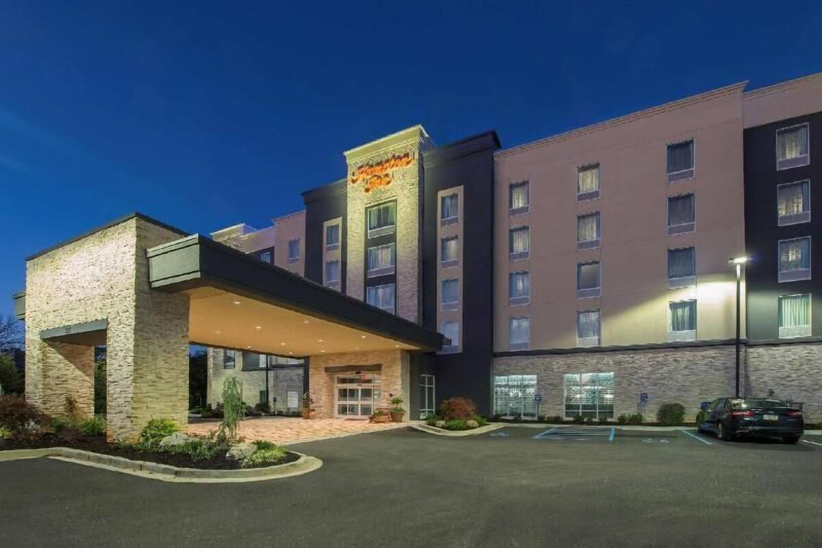 Un hotel con fachada de piedra, un acceso cubierto y un estacionamiento.