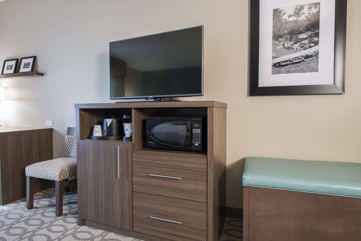 Un espacio habitable compacto con televisión de pantalla plana, microondas, una silla y un mueble pequeño.
