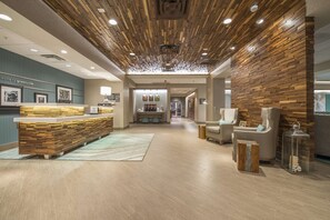 Un área de recepción con un mostrador de madera, una sala de espera con sillas y una pared decorada con cuadros enmarcados.