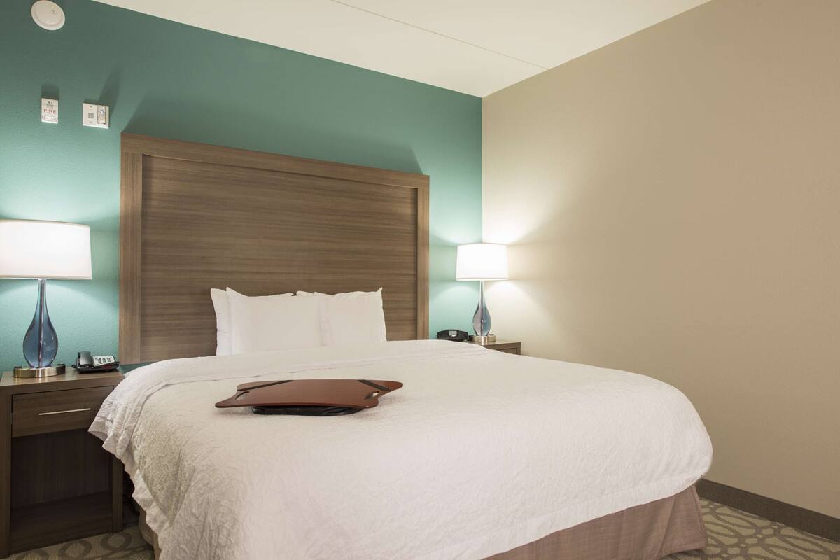 Habitación de hotel con una cama grande, dos lámparas de noche, una mesita de noche y un detector de incendios en la pared.