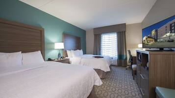 A hotel room with two beds, a TV, a desk, and a window with curtains.