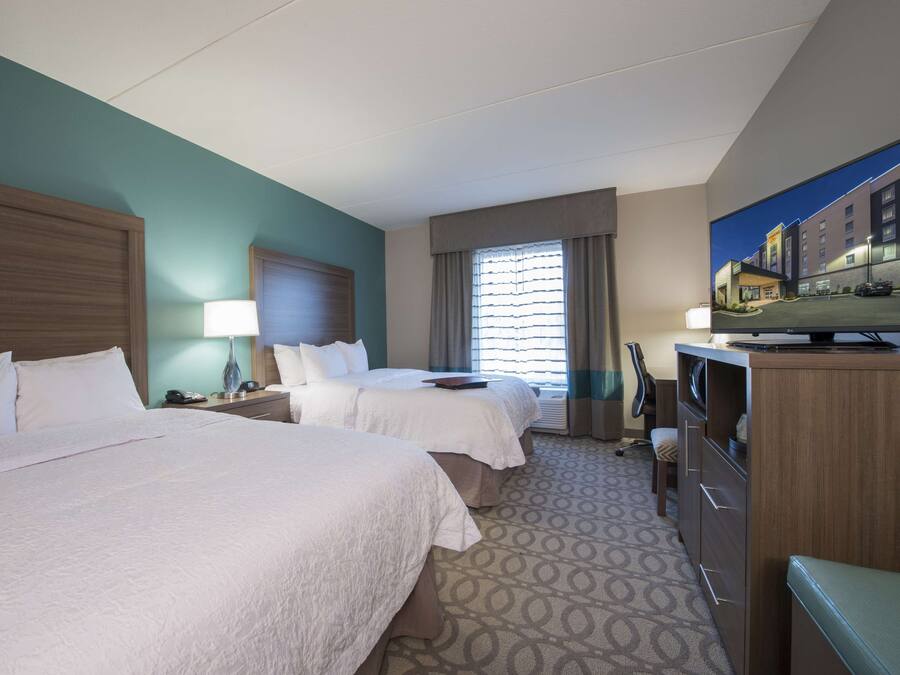 A hotel room with two beds, a TV, a desk, and a window with curtains.