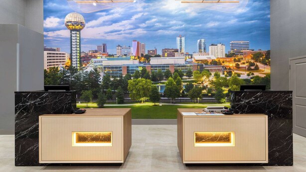 A reception area with a cityscape mural, two reception desks, and a modern design. - La Quinta Inn & Suites by Wyndham Knoxville Papermill (Knoxville)