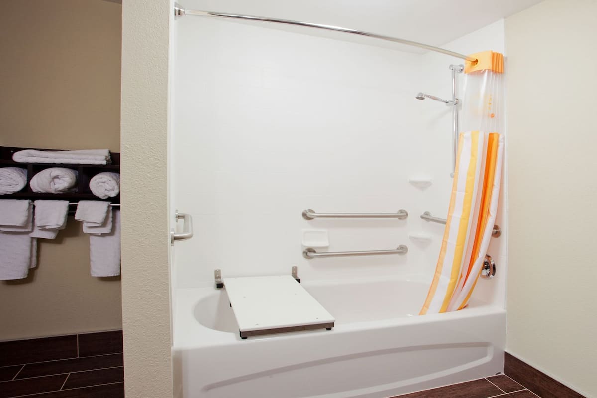 A modern bathroom with a bathtub, grab bars, and a towel rack.