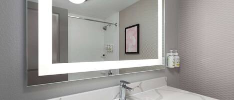 Un baño moderno con un espejo grande, lavabo de mármol blanco y zona de ducha.