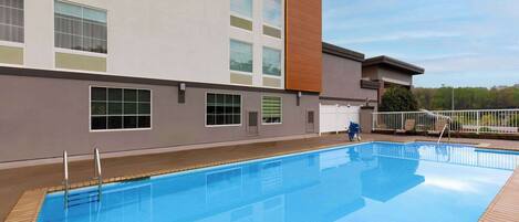 Una piscina junto a un edificio de hotel con múltiples ventanales y un panel decorativo de madera.