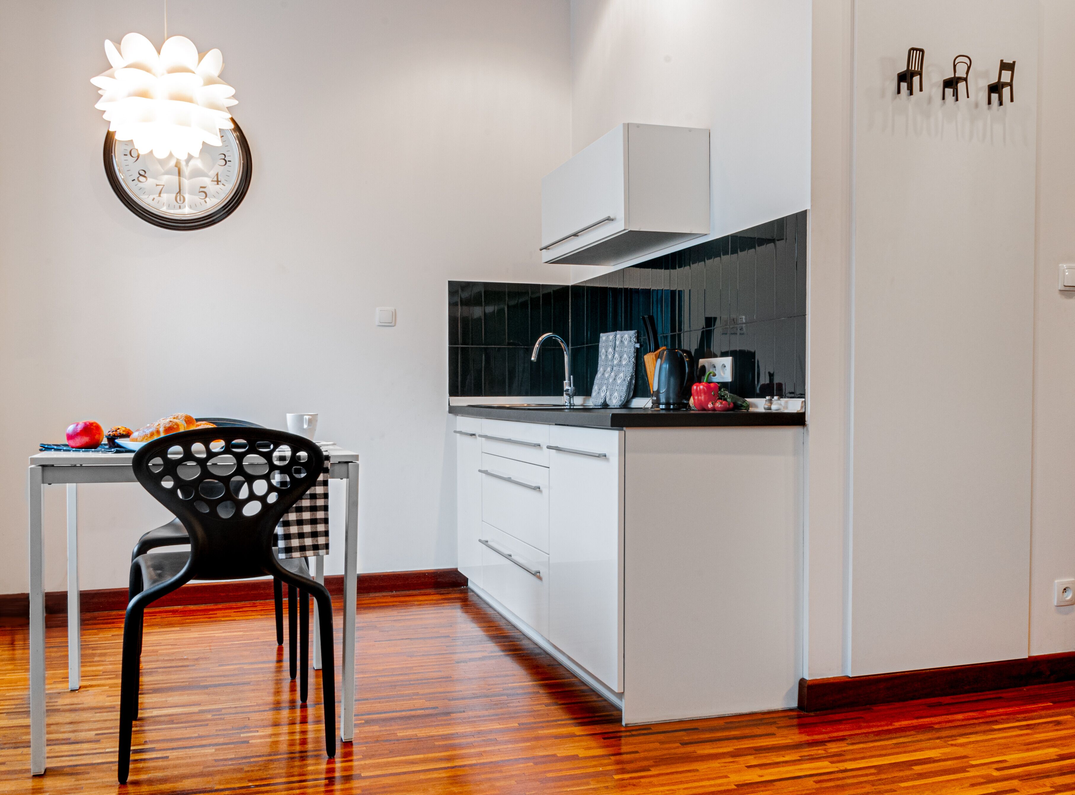 Una cucina moderna con mobili bianchi, un piano di lavoro nero e un pavimento in legno.